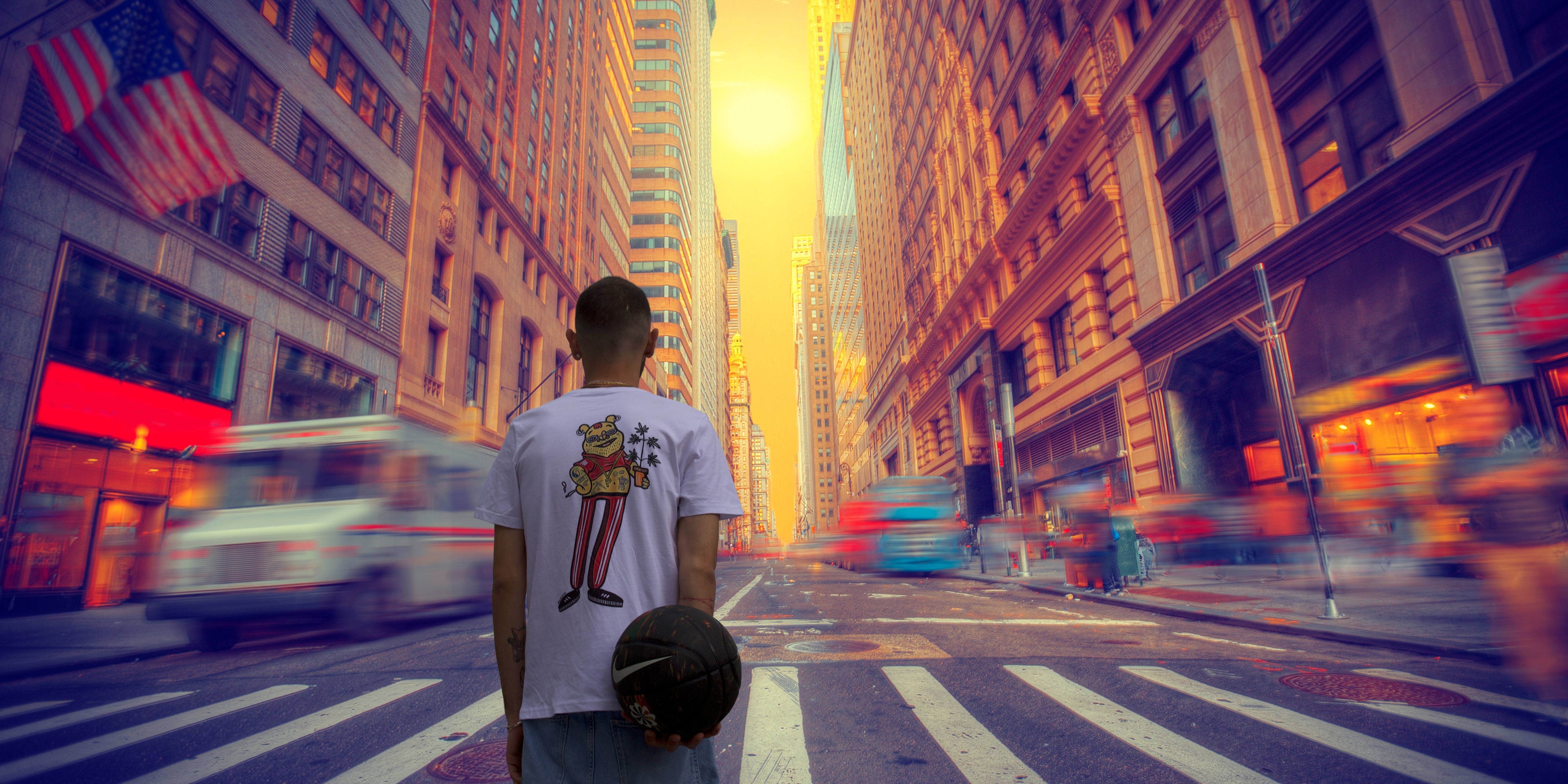 A man wearing a limited editionT-Shirt from 99things.ch carrying a basketball standing in the street of a city