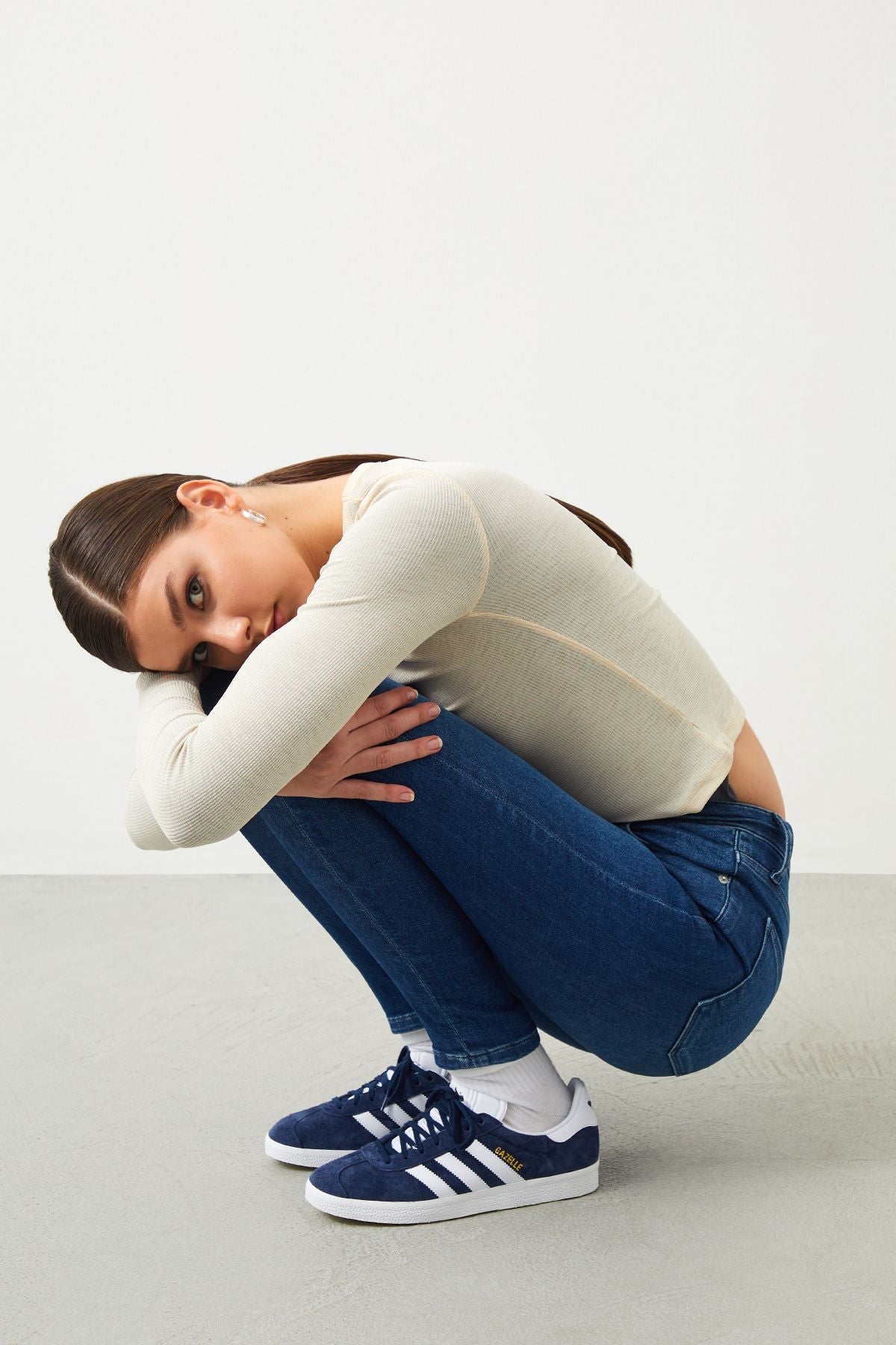 a woman sitting on the ground with her hands on her knees wearing a slim medium blue jeans highlighting the great fit.