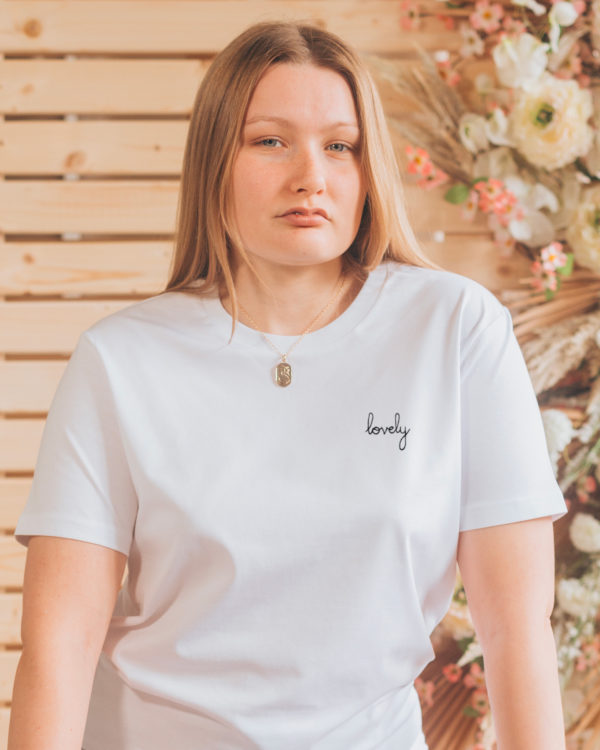 A woman wears a chic white tee adorned with black 'lovely' embroidery