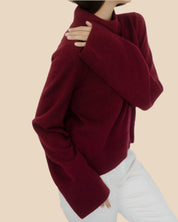 Side angle of a women’s burgundy cashmere sweater by Nuage Cashmere, showcasing its wide, long sleeves and lightweight, cozy design in a deep red shade.