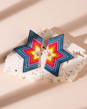 Close-up of a pair of large, red and emerald beaded earrings in a half-star shape, with vibrant beads creating a stunning gradient effect.