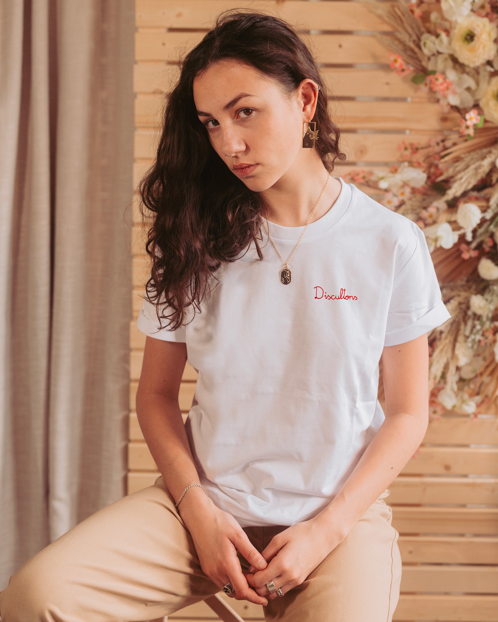 Woman in crisp white T-shirt, seated elegantly, showcasing 'Discultons' in vibrant red hand-embroidery.