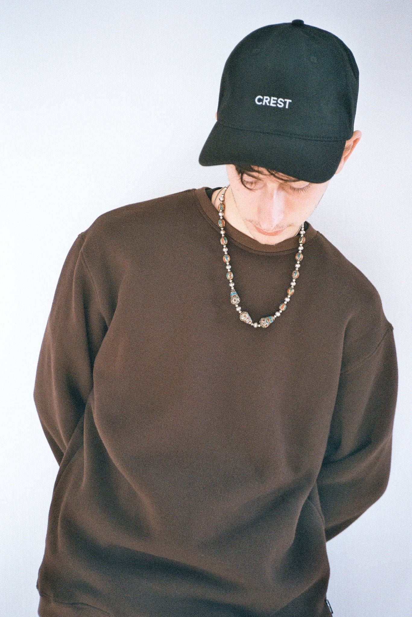 Young man wearing a chocolate brown sweatshirt from Crest styled with a cap and jewellery