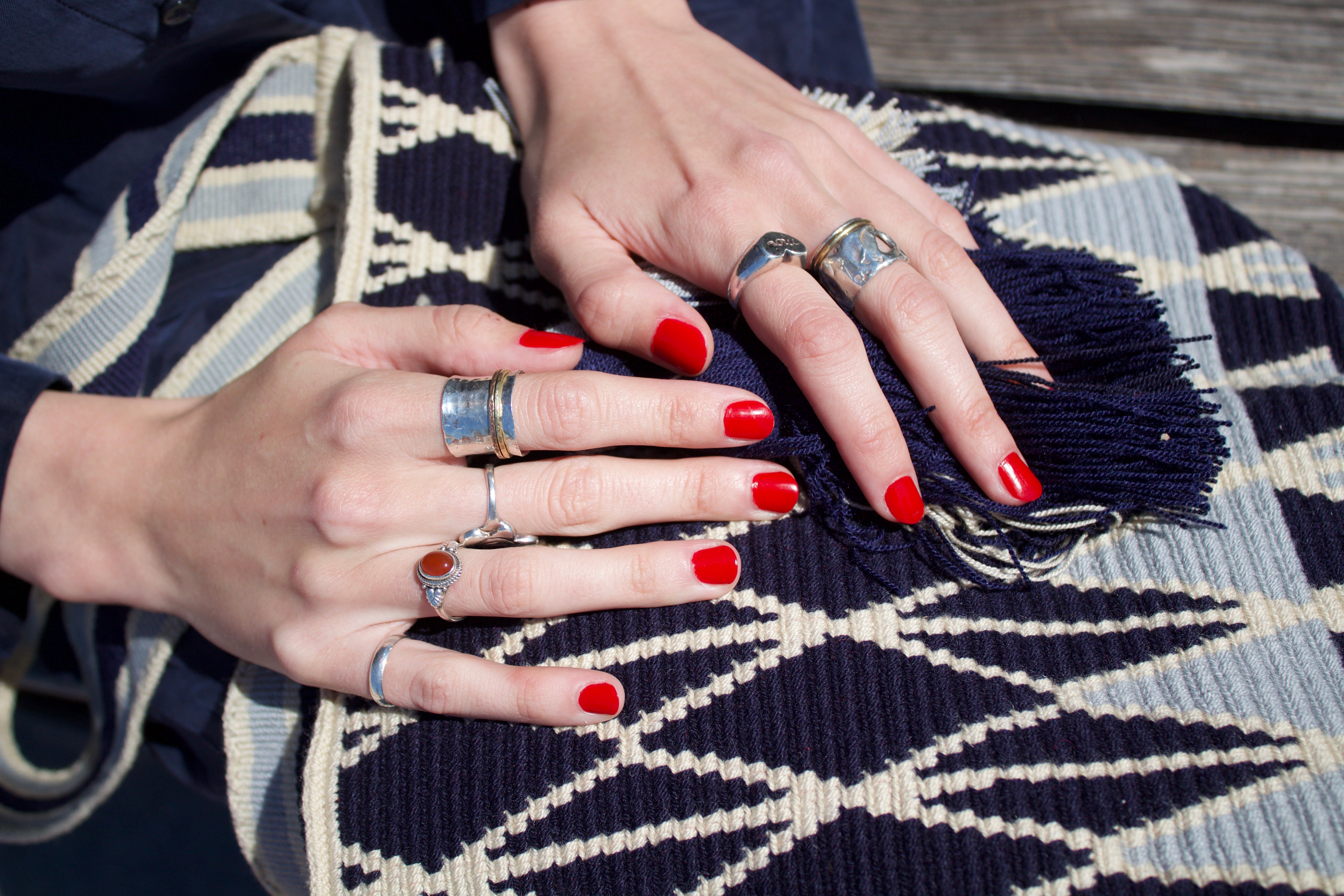 Women's hands with red nails and silver rings holding a handwoven Wayuu bag