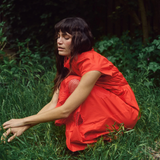 Model leaning wearing MMAria Mono Dress in Soft Coral, flowing midi-length skirt