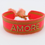 Close-up of adjustable neon orange woven friendship bracelet with green border and gold embroidered "AMORE" lettering and sliding knot cords.