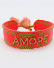 Close-up of adjustable neon orange woven friendship bracelet with green border and gold embroidered "AMORE" lettering and sliding knot cords.
