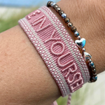 Close-up of adjustable vintage rose woven bracelet with embroidered “BELIEVE IN YOURSELF” lettering and sliding knot tassel cords.
