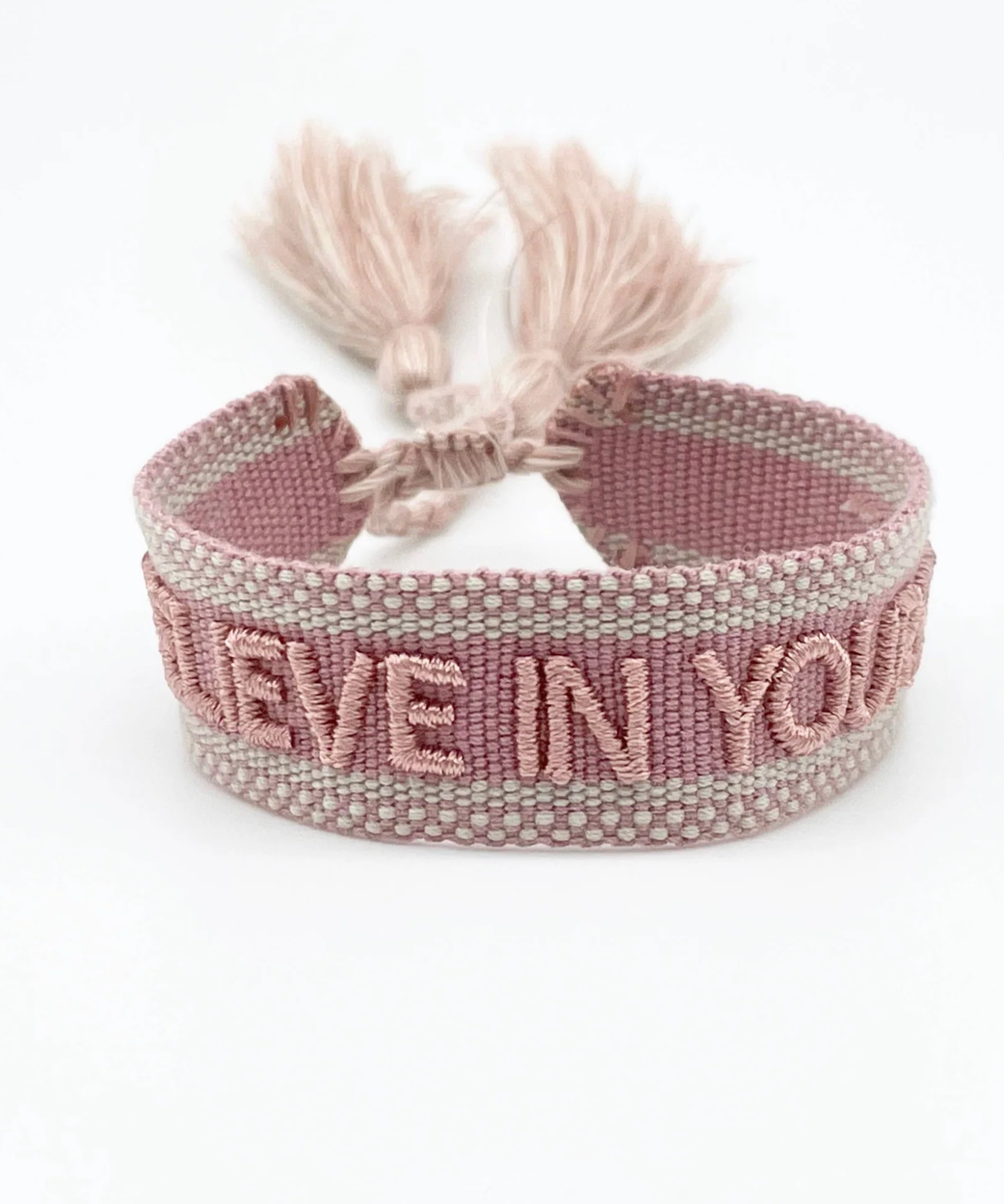 Close-up of adjustable vintage rose woven bracelet with embroidered “BELIEVE IN YOURSELF” lettering and sliding knot tassel cords.