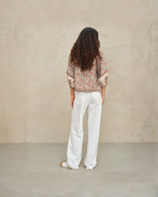 Model wearing a Della shirt and white pants against a beige wall