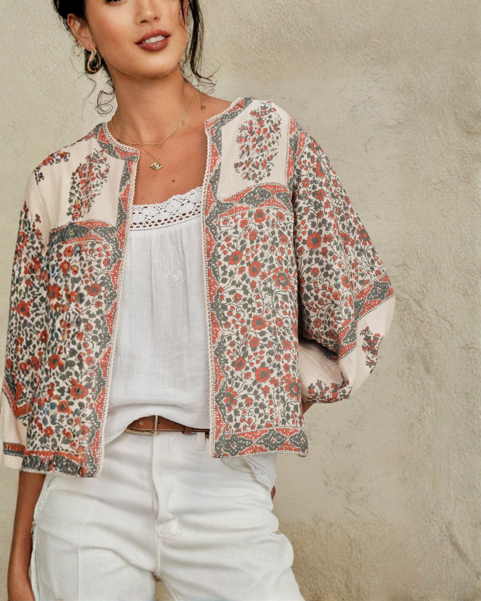 Woman wearing Della jacket over a white top and pants against a neutral background