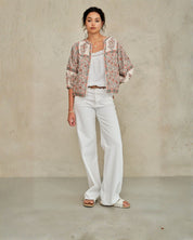 Model wearing a Della jacket, white top, and pants against a plain background