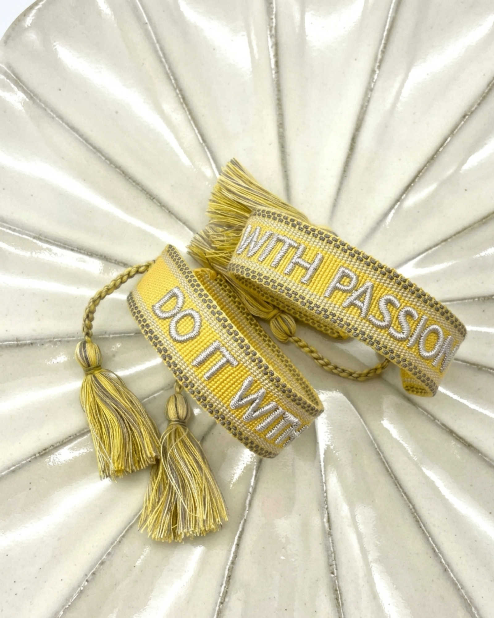 Close-up of adjustable sunshine yellow woven bracelet with embroidered “DO IT WITH PASSION” lettering and sliding knot tassel cords.