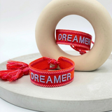 Close-up of adjustable coral red woven bracelet with embroidered “DREAMER” lettering and sliding knot tassel cords.
