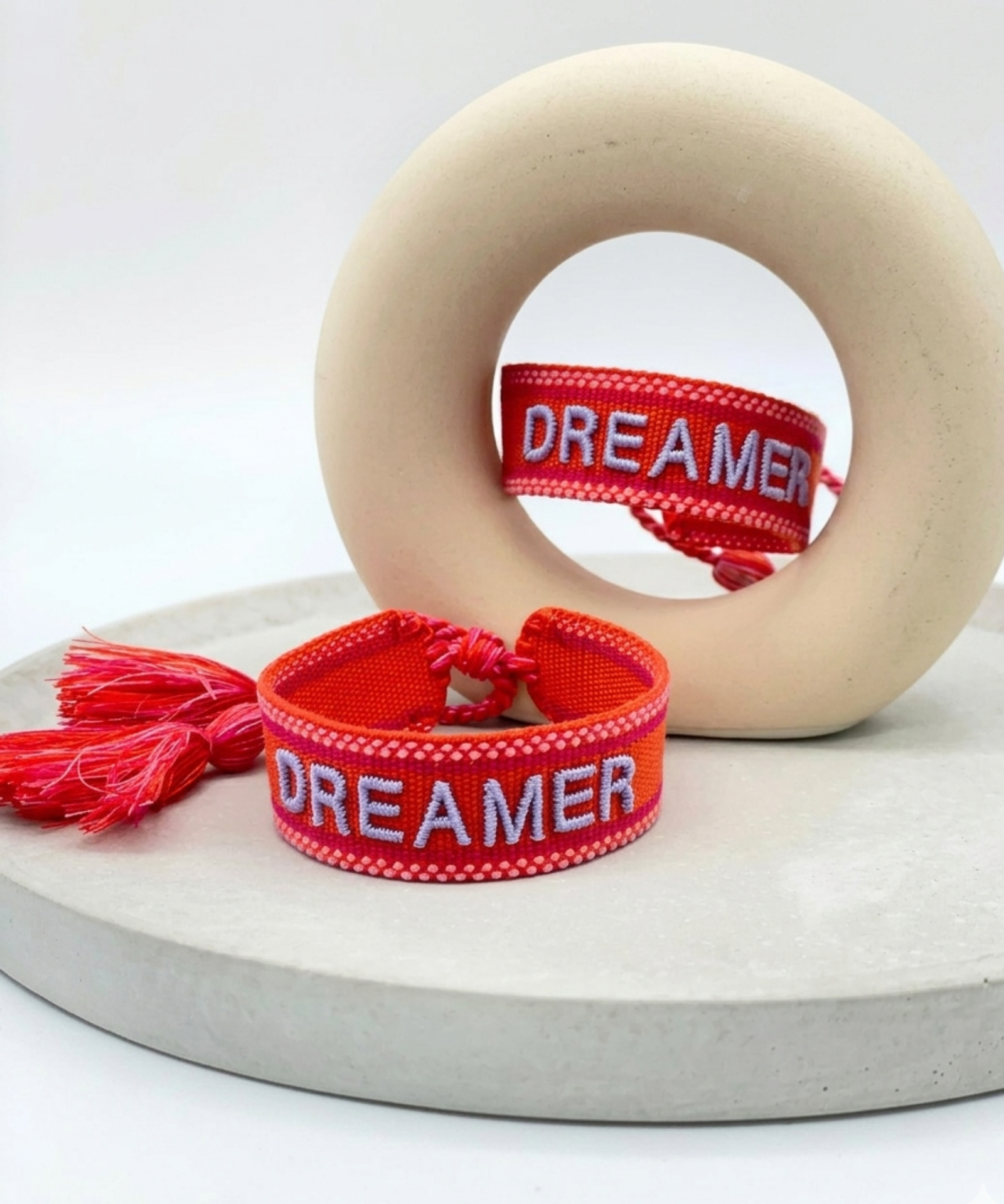 Close-up of adjustable coral red woven bracelet with embroidered “DREAMER” lettering and sliding knot tassel cords.