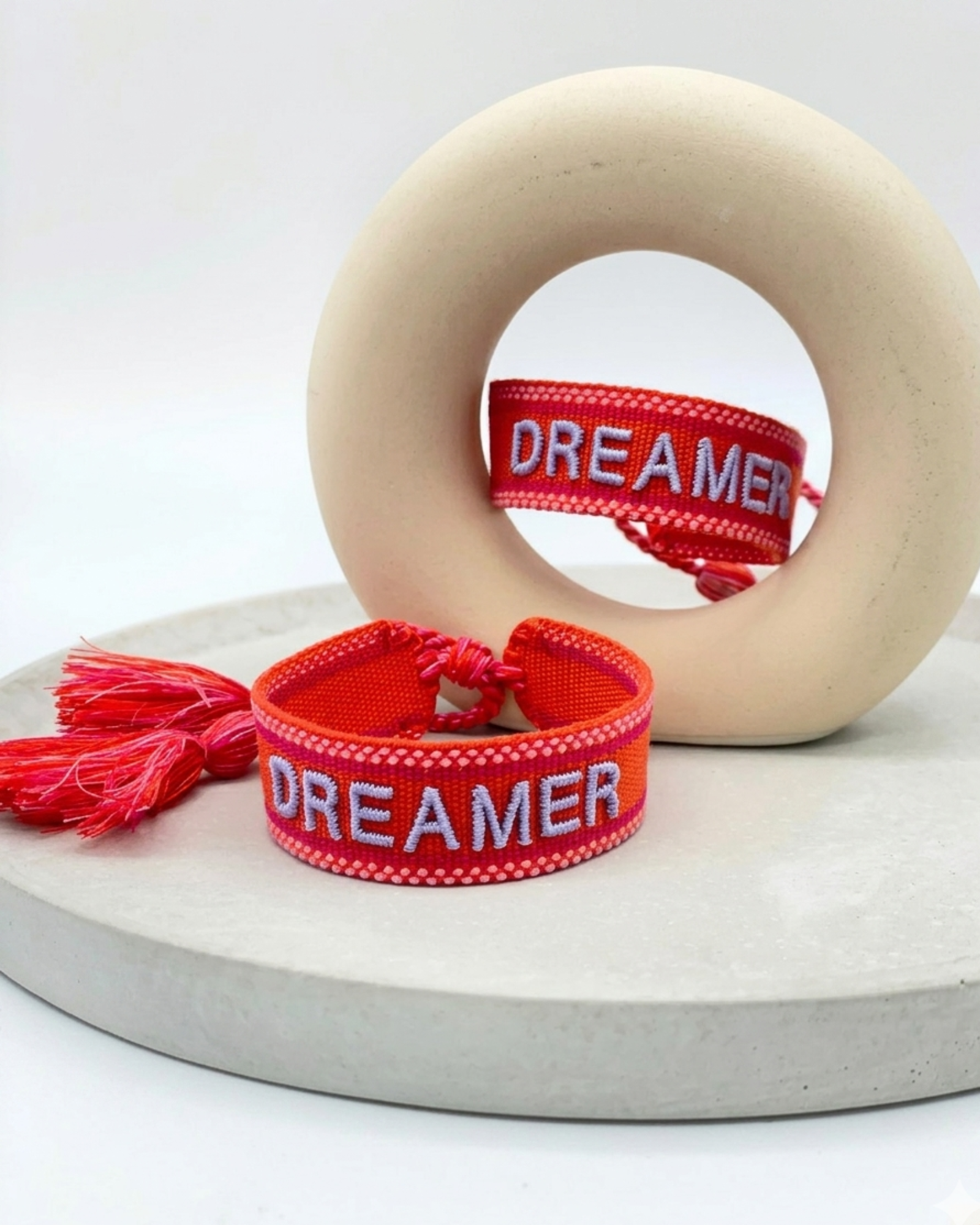 Close-up of adjustable coral red woven bracelet with embroidered “DREAMER” lettering and sliding knot tassel cords.