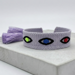 Close-up of adjustable lavender woven bracelet featuring embroidered evil eye talisman design with sliding knot tassel cords.