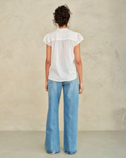 Person wearing a white blouse and blue jeans against a plain background