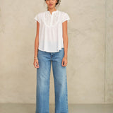 Woman wearing a white blouse and blue jeans against a plain background