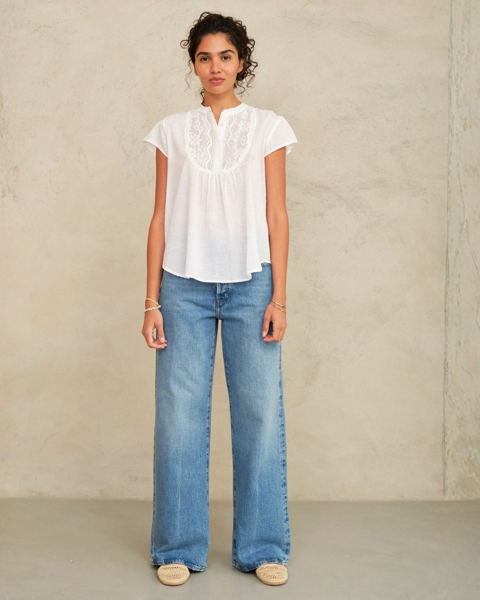 Woman wearing a white blouse and blue jeans against a plain background