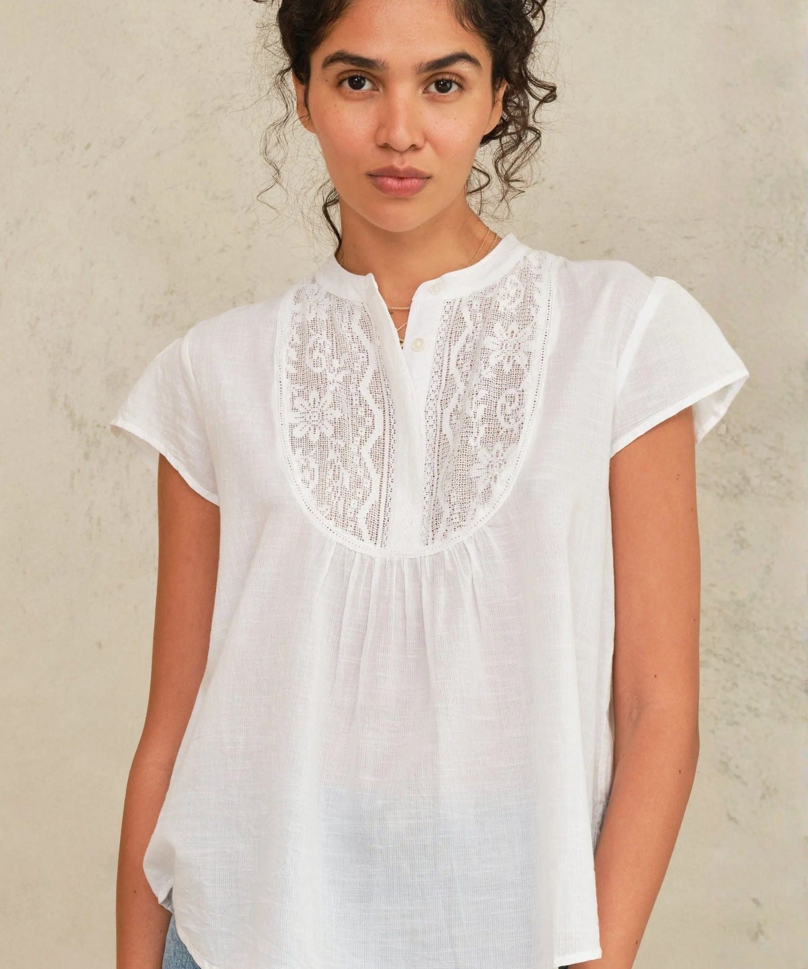 Woman wearing a white blouse with lace details against a neutral background