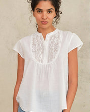Woman wearing a white blouse with lace details against a neutral background