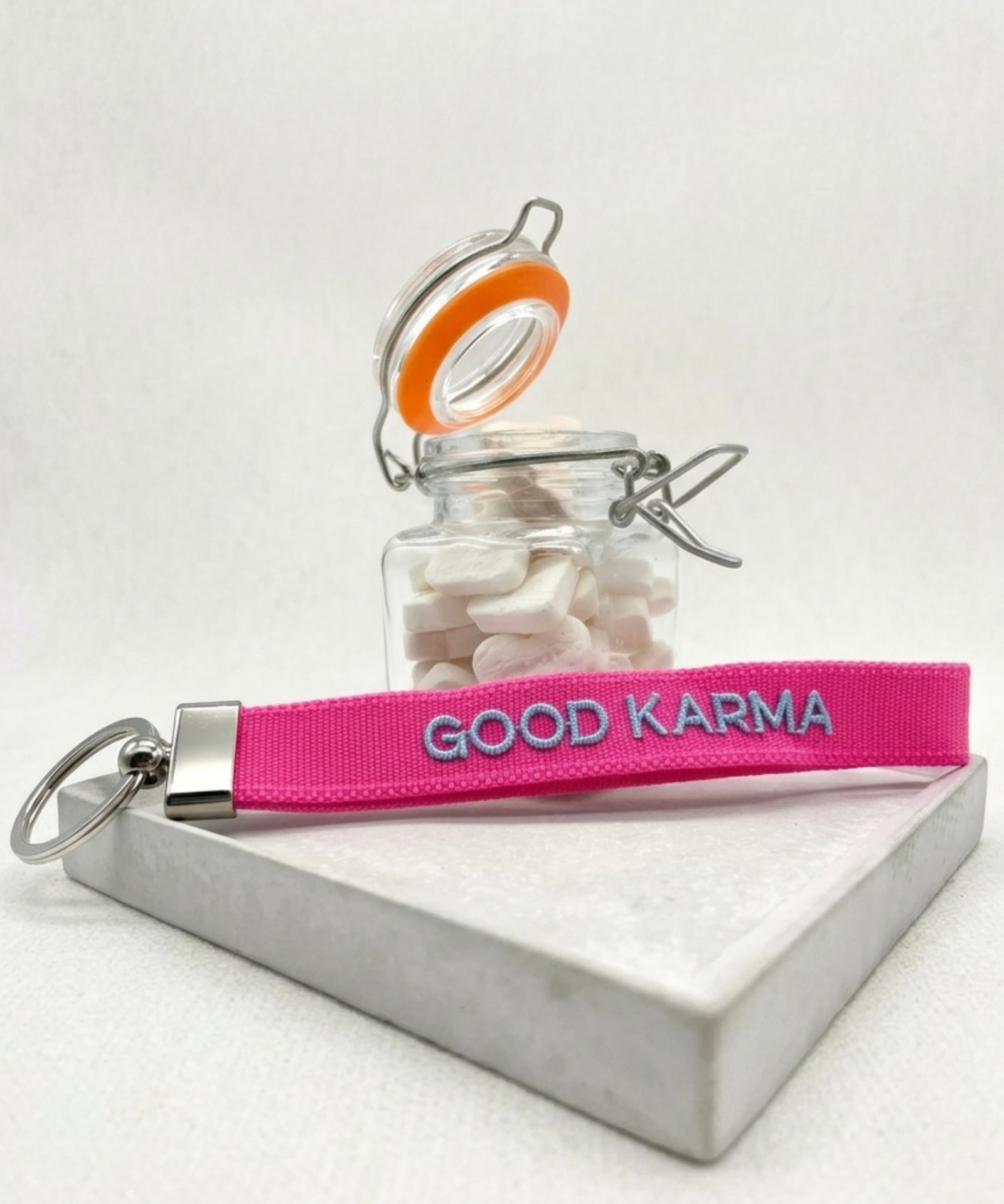 Close-up of embroidered pink woven keychain with blue “GOOD KARMA” text and silver metal keyring on a tightly woven strap.