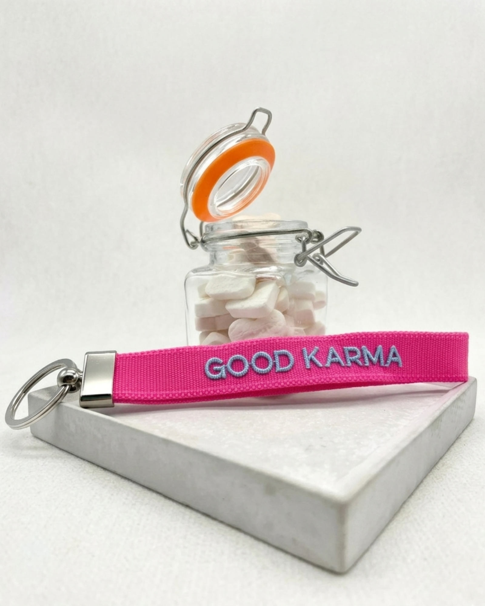 Close-up of embroidered pink woven keychain with blue “GOOD KARMA” text and silver metal keyring on a tightly woven strap.