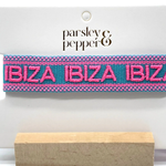 Close-up of adjustable turquoise woven friendship bracelet with pink border and embroidered "IBIZA IBIZA IBIZA" lettering with sliding knot cords.