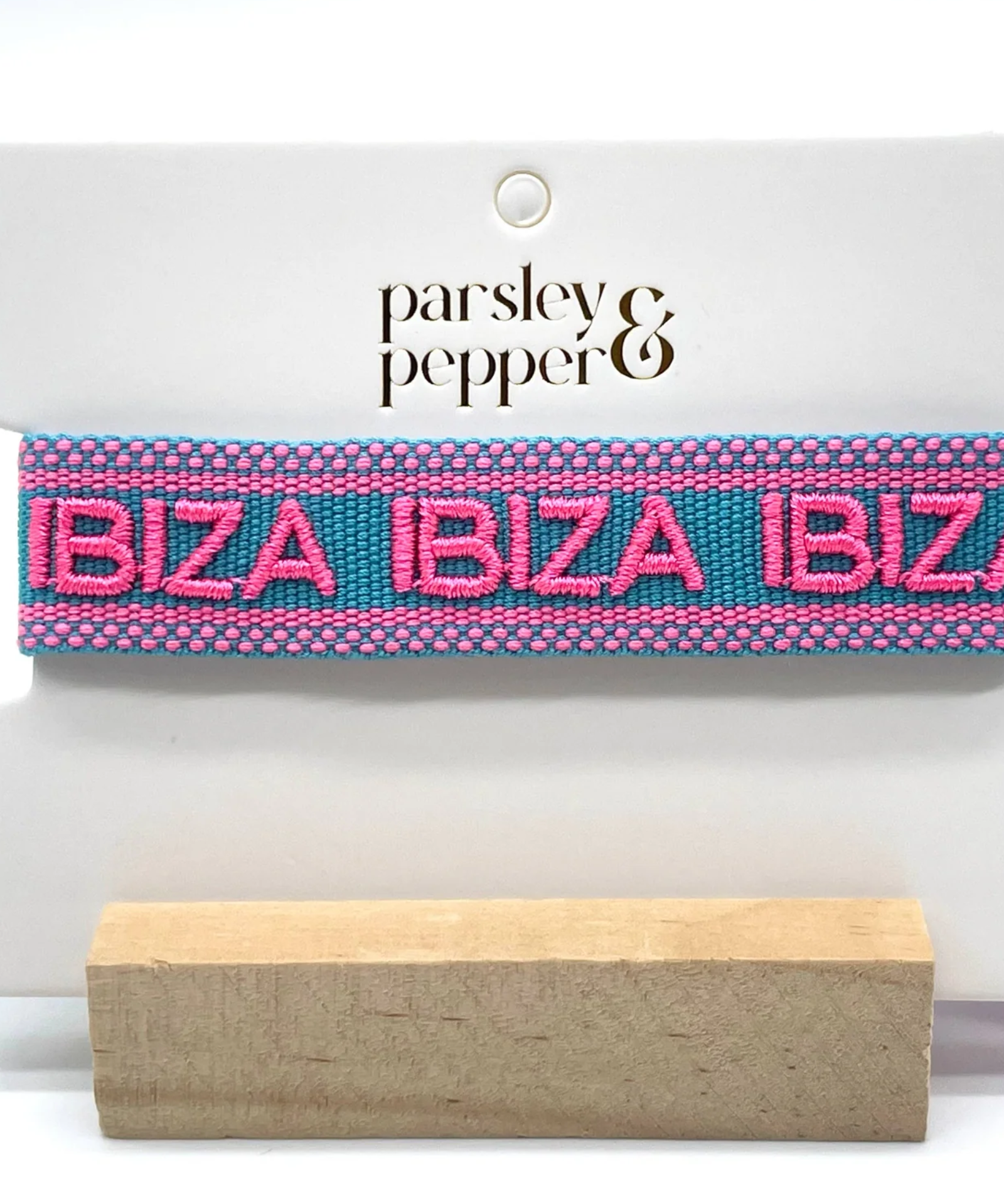 Close-up of adjustable turquoise woven friendship bracelet with pink border and embroidered "IBIZA IBIZA IBIZA" lettering with sliding knot cords.