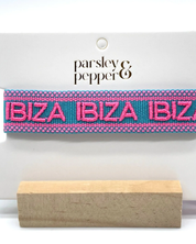 Close-up of adjustable turquoise woven friendship bracelet with pink border and embroidered "IBIZA IBIZA IBIZA" lettering with sliding knot cords.