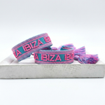 Close-up of adjustable turquoise woven friendship bracelet with pink border and embroidered "IBIZA IBIZA IBIZA" lettering with sliding knot cords.