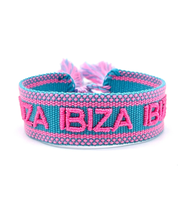 Close-up of adjustable turquoise woven friendship bracelet with pink border and embroidered "IBIZA IBIZA IBIZA" lettering with sliding knot cords.
