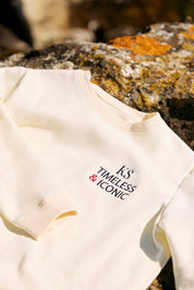 Close-up of the soft ecru fabric and embroidered 'TIMELESS' and 'ICONIC' detailing.