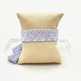 Close-up of adjustable purple and cream jacquard woven friendship bracelet with lilac embroidered “J’ADORE” lettering and sliding knot tassel cords.