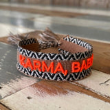 Close-up of adjustable woven boho friendship bracelet with neon orange “Karma, Baby!” embroidery and sliding tassel cords on a brown woven band.
