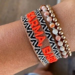 Close-up of adjustable woven boho friendship bracelet with neon orange “Karma, Baby!” embroidery and sliding tassel cords on a brown woven band.