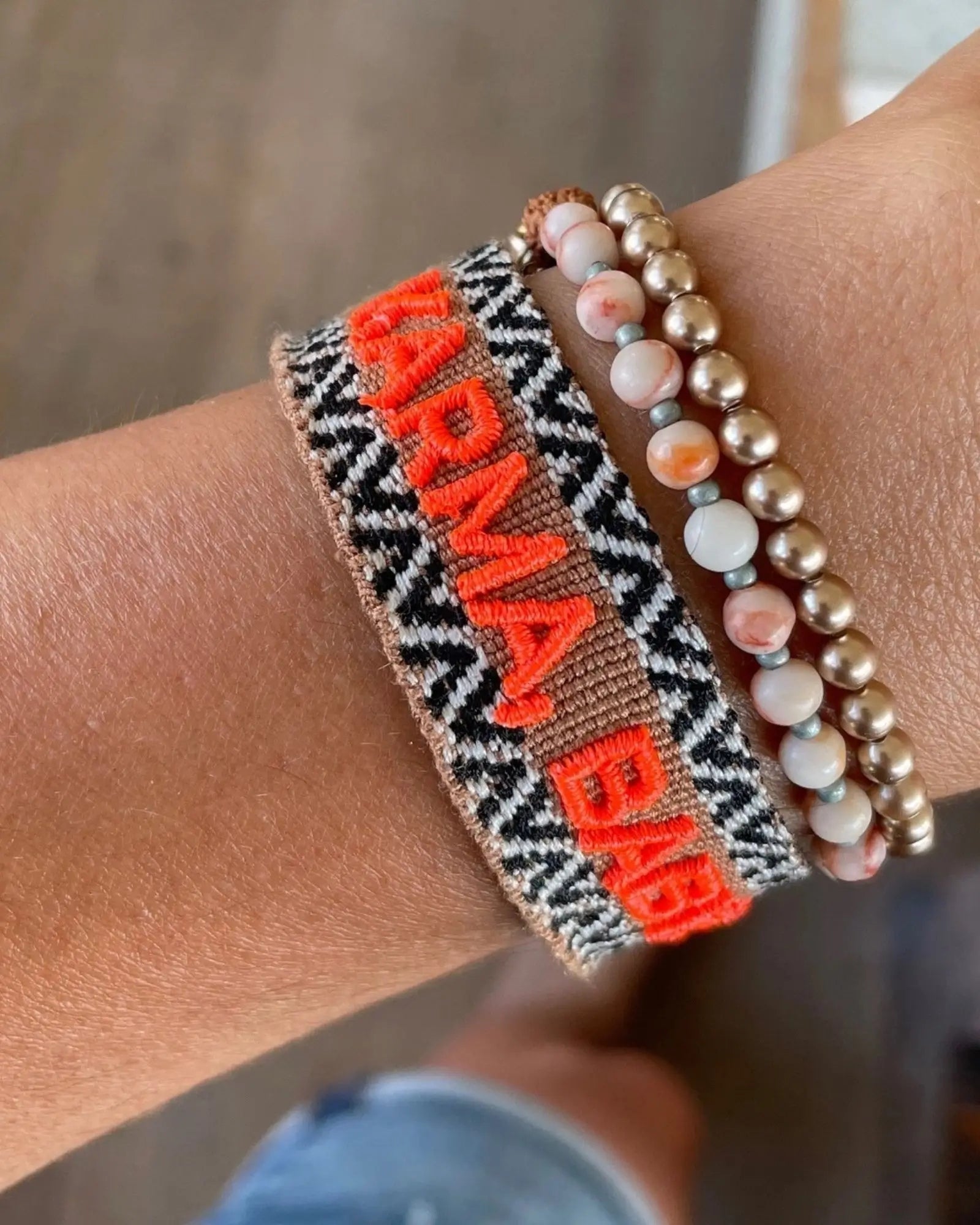 Close-up of adjustable woven boho friendship bracelet with neon orange “Karma, Baby!” embroidery and sliding tassel cords on a brown woven band.