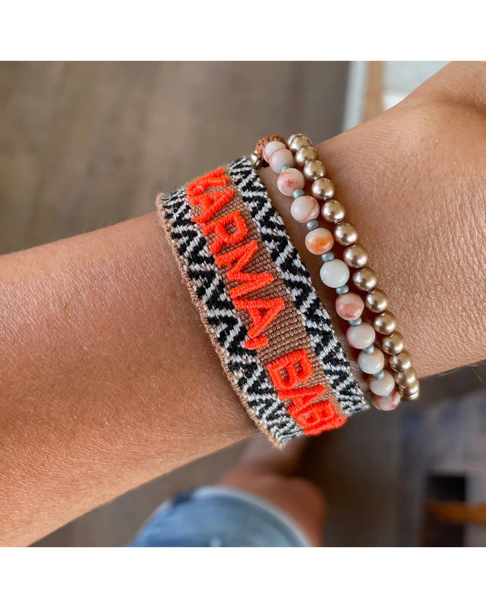 Close-up of adjustable woven boho friendship bracelet with neon orange “Karma, Baby!” embroidery and sliding tassel cords on a brown woven band.