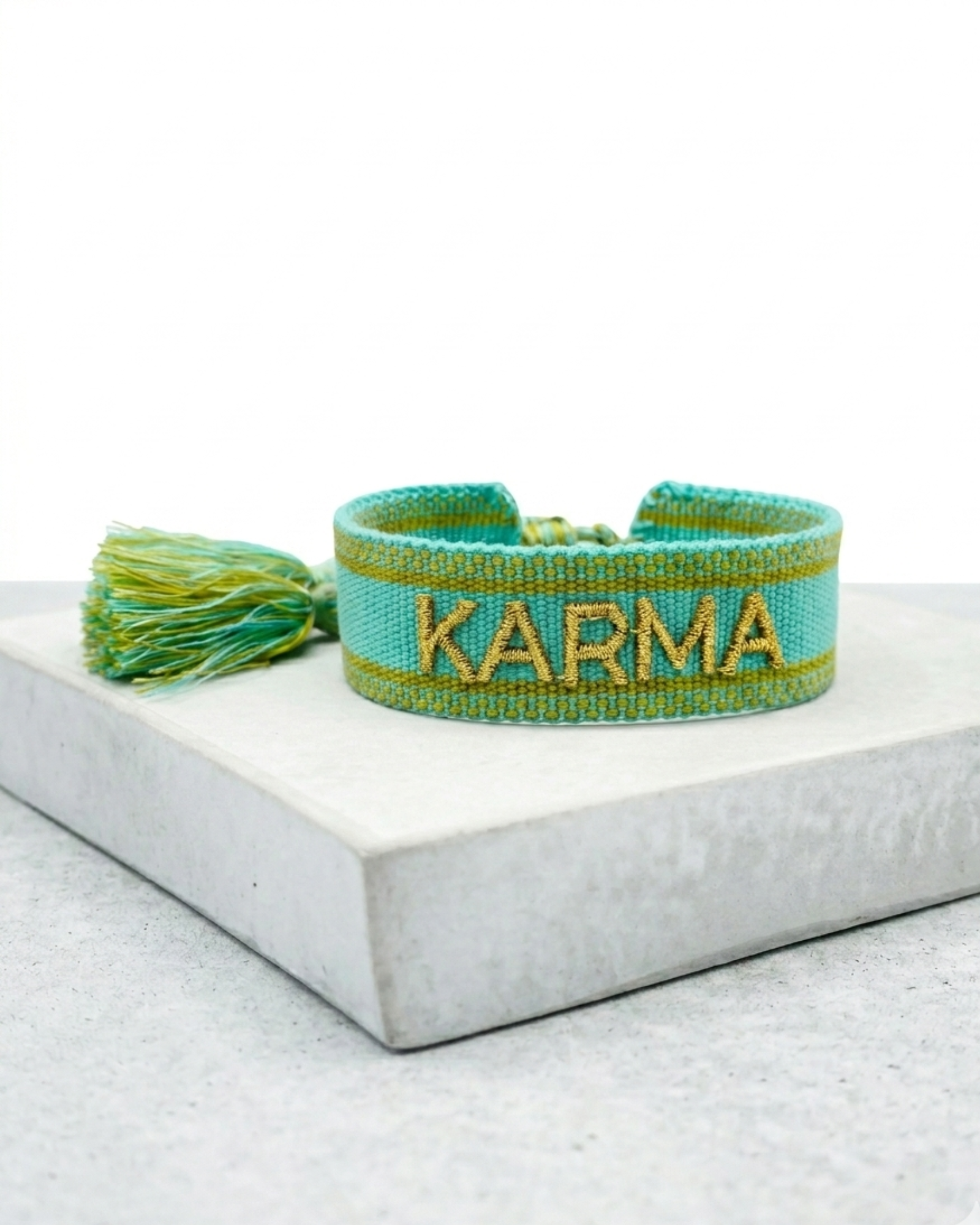 Close-up of adjustable turquoise woven bracelet with gold embroidered “KARMA” lettering and sliding knot tassel cords.