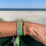 Close-up of adjustable turquoise woven bracelet with gold embroidered “KARMA” lettering and sliding knot tassel cords.