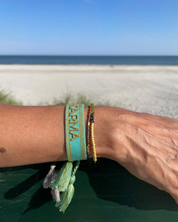 Close-up of adjustable turquoise woven bracelet with gold embroidered “KARMA” lettering and sliding knot tassel cords.