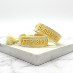Close-up of adjustable yellow sorbet woven bracelet with embroidered “KEEP SMILING” lettering and sliding knot tassel cords.