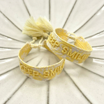 Close-up of adjustable yellow sorbet woven bracelet with embroidered “KEEP SMILING” lettering and sliding knot tassel cords.