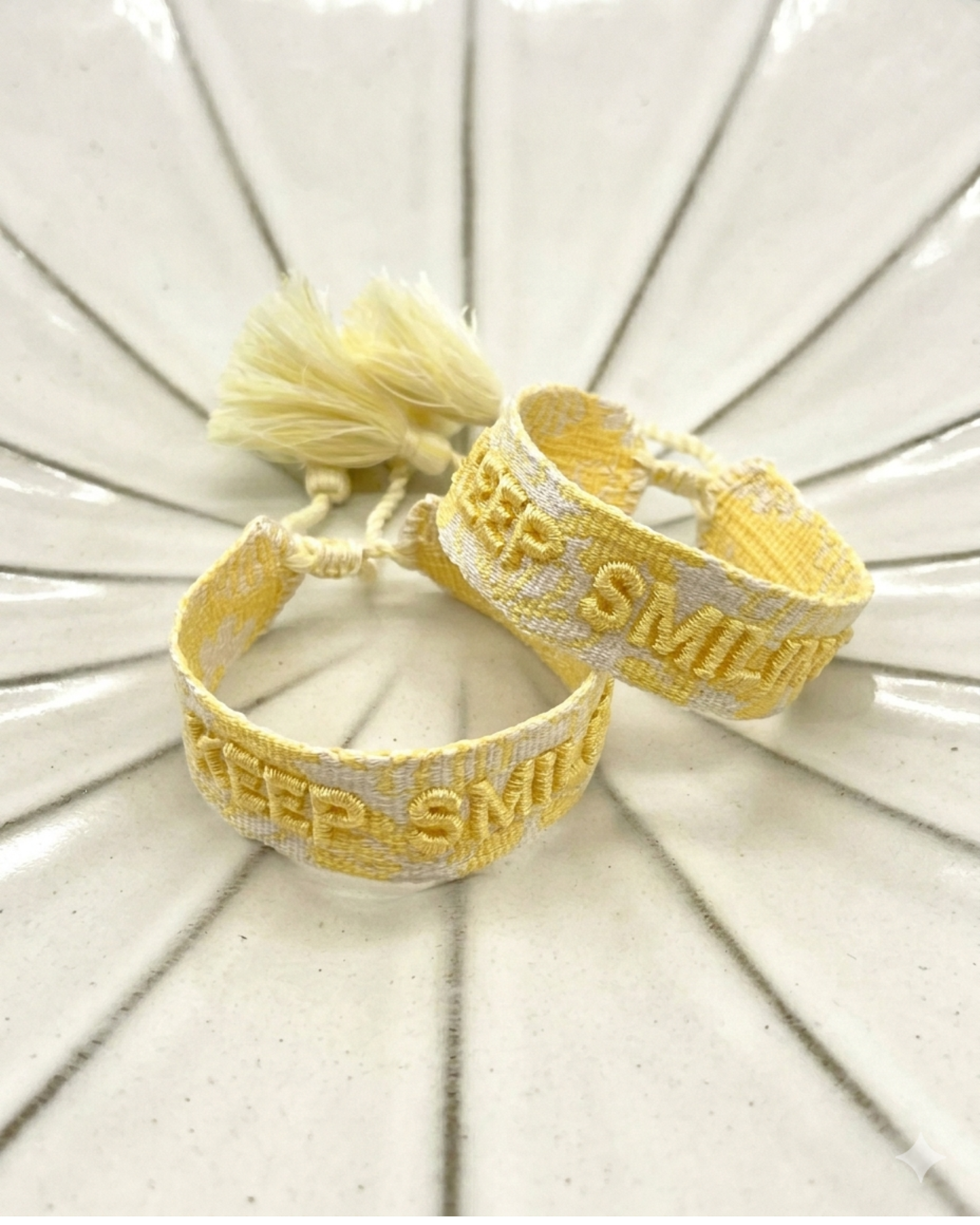 Close-up of adjustable yellow sorbet woven bracelet with embroidered “KEEP SMILING” lettering and sliding knot tassel cords.