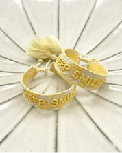 Close-up of adjustable yellow sorbet woven bracelet with embroidered “KEEP SMILING” lettering and sliding knot tassel cords.
