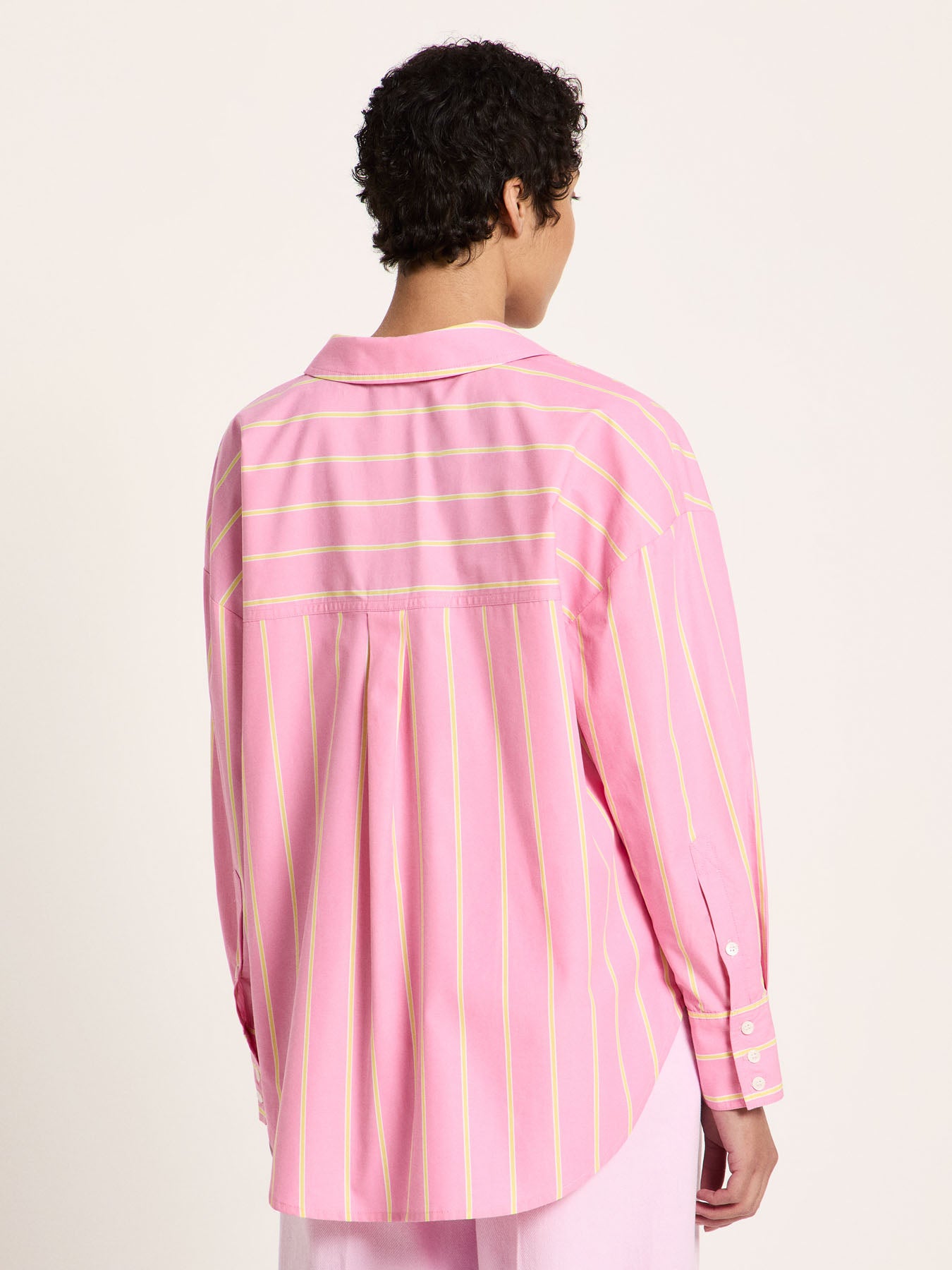 Back view of oversized pink striped shirt on model, box pleat and yoke detail visible.