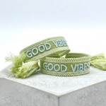 Close-up of adjustable cornflower blue woven bracelet with embroidered “LIVE LOVE SHINE” lettering and sliding knot tassel cords.