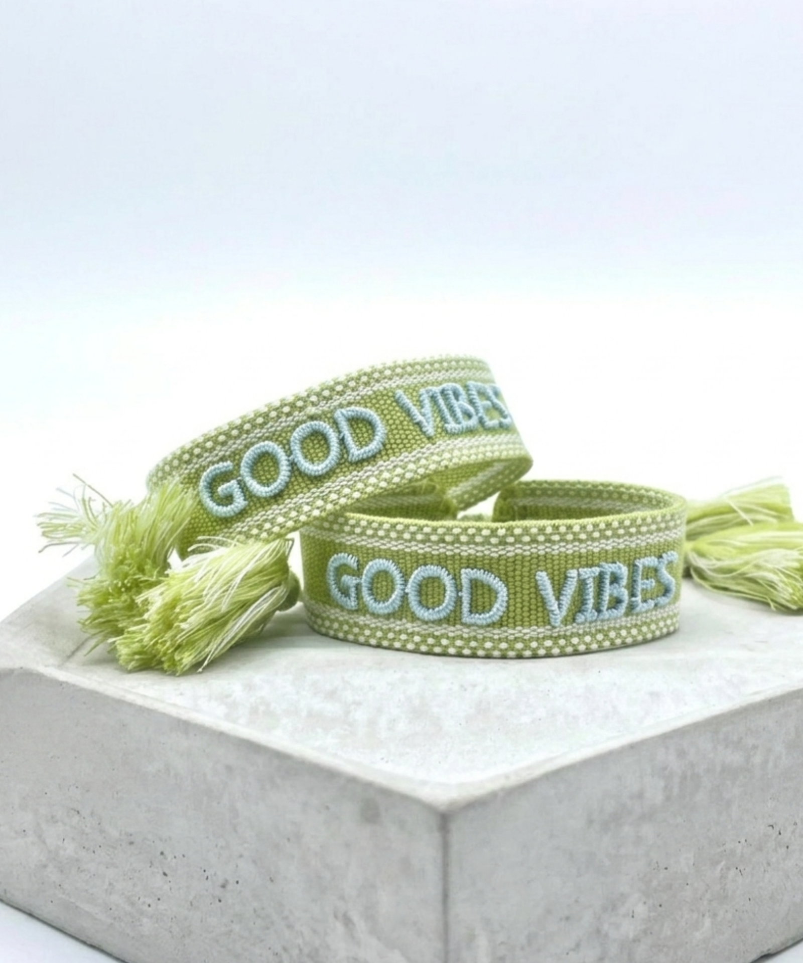 Close-up of adjustable cornflower blue woven bracelet with embroidered “LIVE LOVE SHINE” lettering and sliding knot tassel cords.