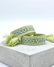 Close-up of adjustable cornflower blue woven bracelet with embroidered “LIVE LOVE SHINE” lettering and sliding knot tassel cords.